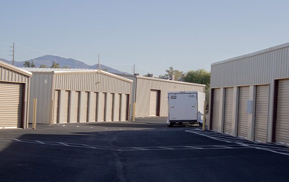 trailer in tow driving past small storage units in wide aisle, secure storage facility